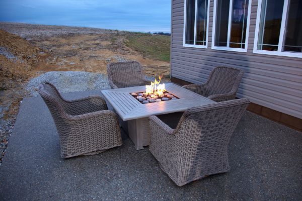 Patio fire table with four wicker chairs beside a house at dusk