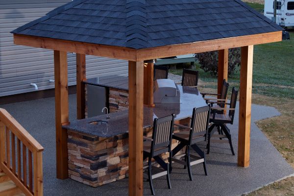 Wooden gazebo with a shingled roof and outdoor dining chairs on a patio at dusk