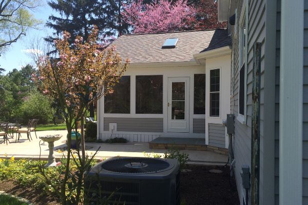 Backyard patio beside a gray house with a screened porch and pink flowering tree.