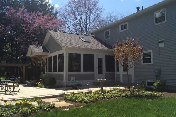 Backyard patio beside a gray house, with a screened porch, stone path, lawn, and pink flowering trees