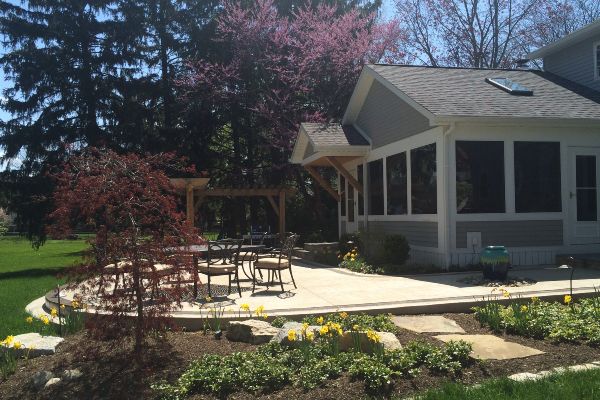 Patio with outdoor tables beside a sunroom and flower beds in a garden yard