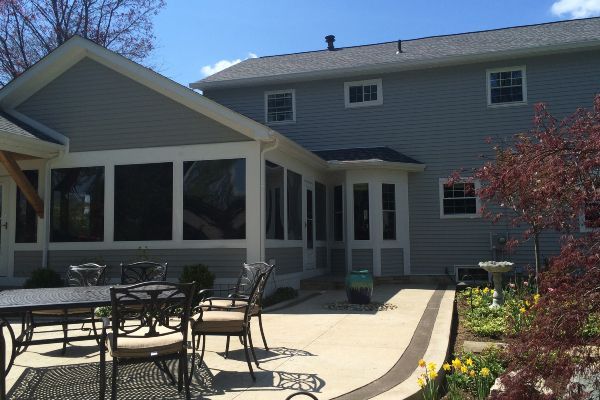 Backyard patio with tables and chairs beside a gray house and covered porch