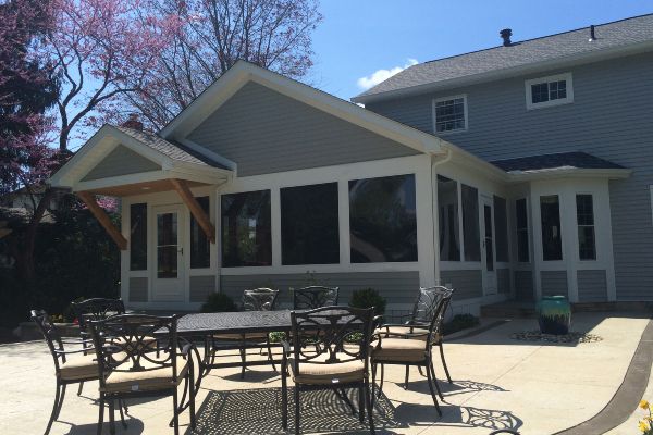Patio with metal tables and chairs outside a house with screened porch and gabled roof