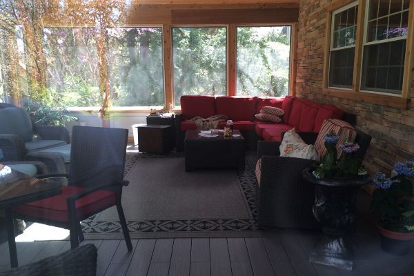 Sunroom with red sectional sofa, black chairs, plants, and large windows overlooking trees