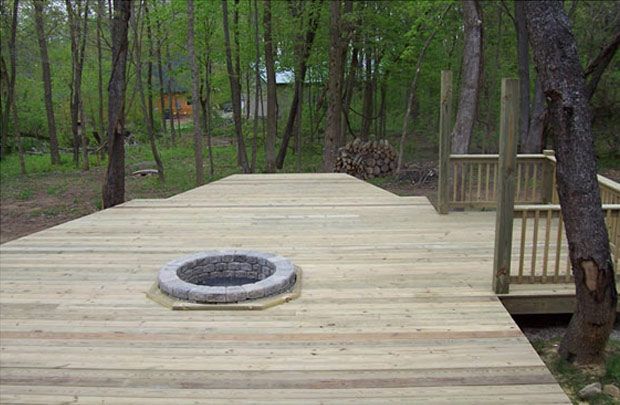 Wooden deck with a circular fire pit surrounded by trees in a wooded backyard