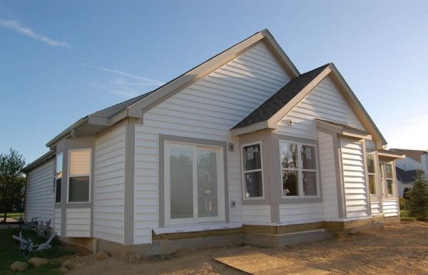 White single-story house with gabled roof and front porch in a dirt lot under clear sky