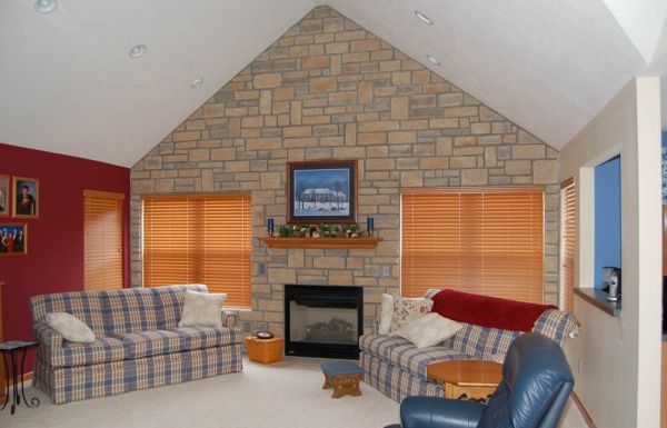 Living room with stone fireplace, plaid sofas, blue chair, and orange blinds under a vaulted ceiling
