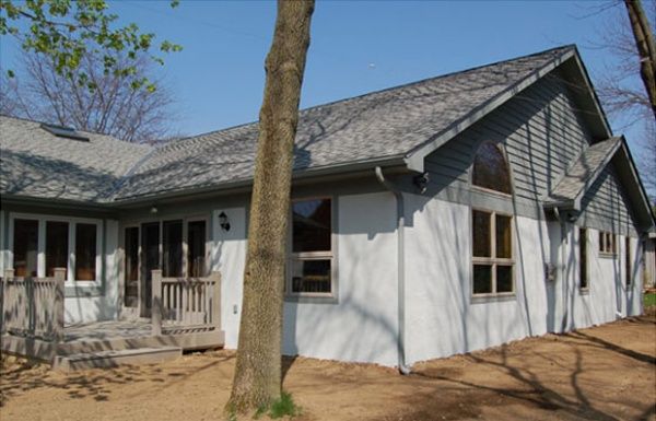 Single-story white house with gray roof, front porch, and a tree in the yard