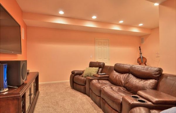 Cozy basement media room with brown leather sectional, carpet, and TV cabinet under recessed lights