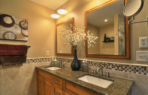 Bathroom vanity with granite countertop, wood cabinets, mirror, and decorative vase of white flowers.