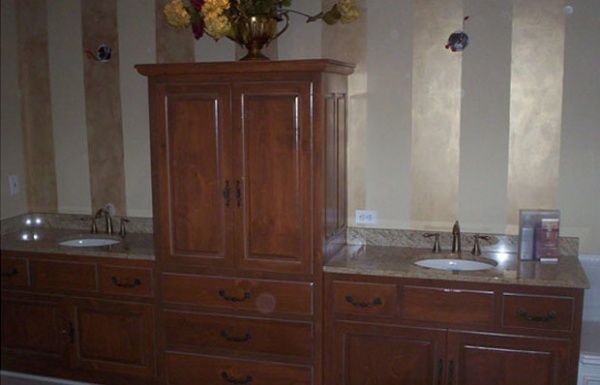 Wooden bathroom vanity with double sinks, mirror, and cabinets against striped walls.