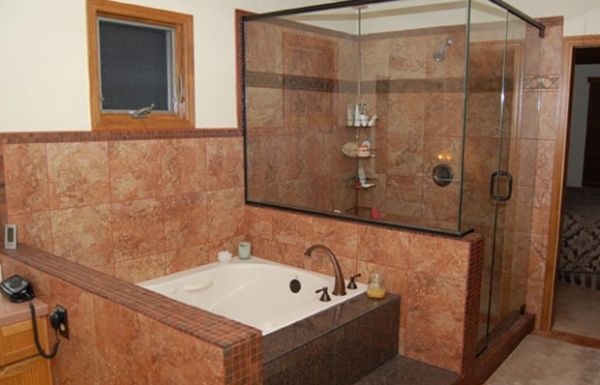 Bathroom with a sunken tub, glass shower enclosure, and tan tile walls and floor