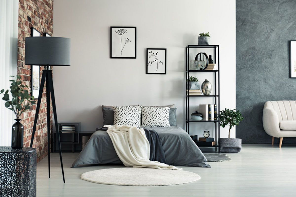 Minimalist bedroom with gray bed, white rug, black floor lamp, and framed wall art