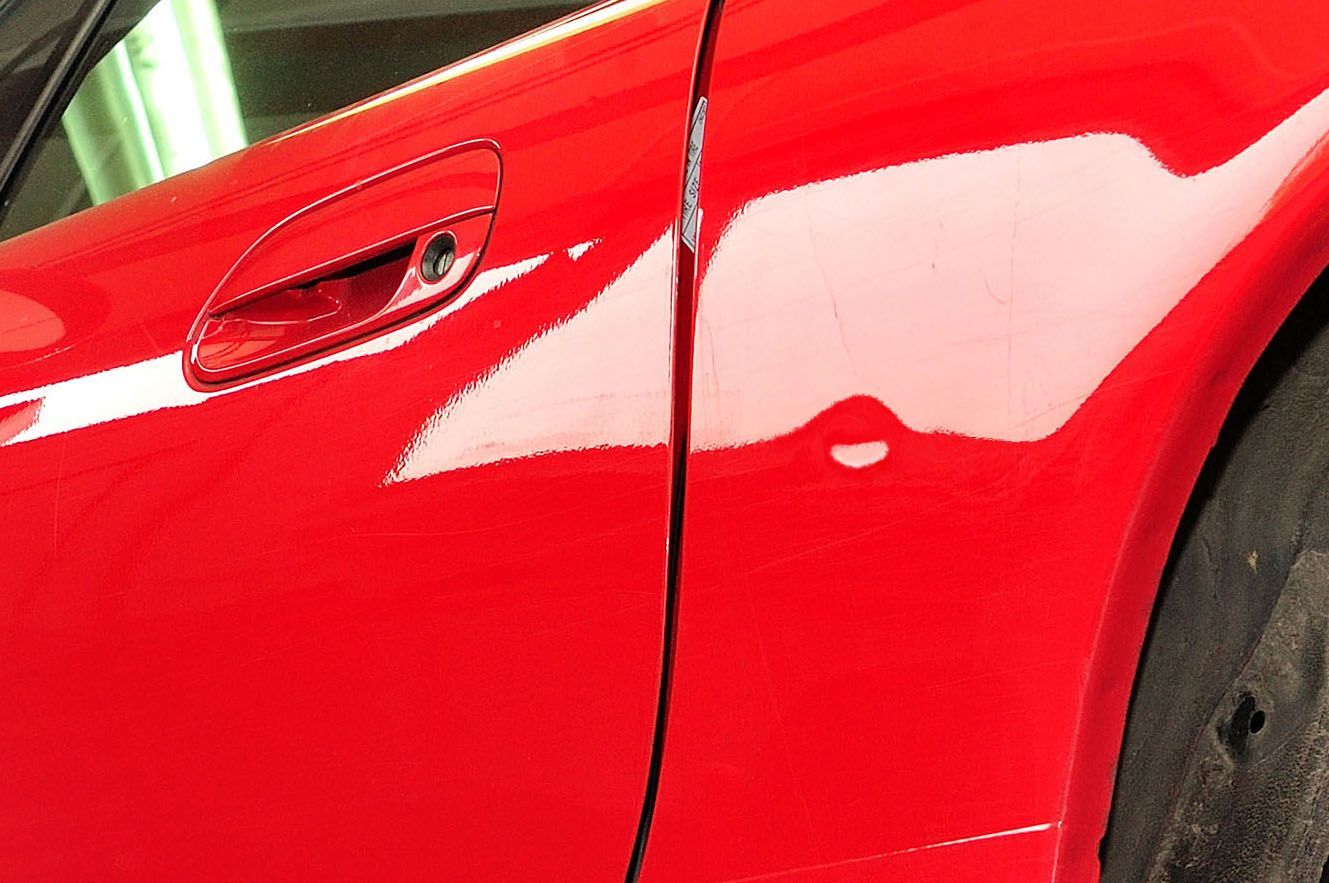 A close-up view of the side of a glossy red car, showing the seam between the door and the rear quarter panel.