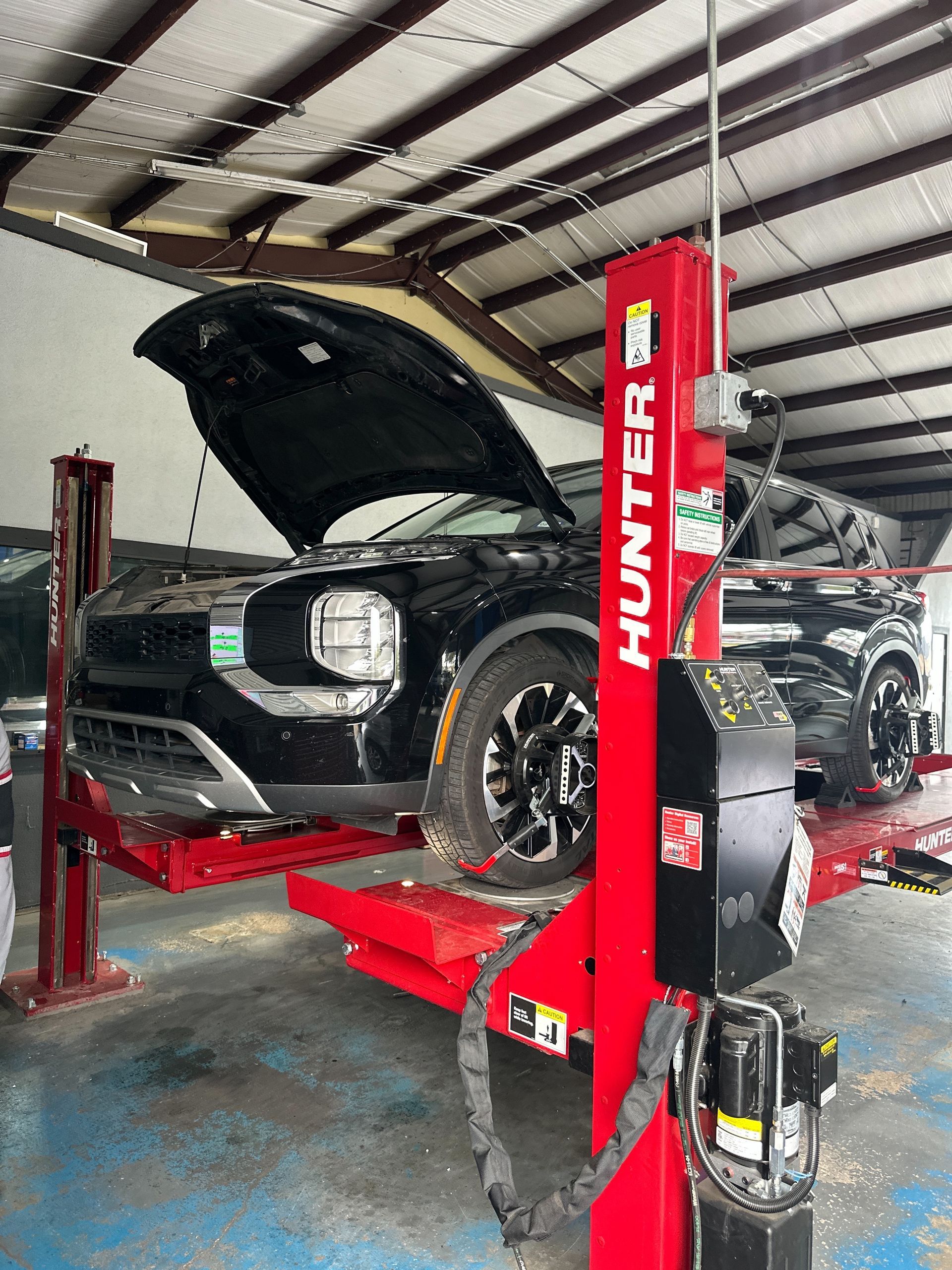 A black SUV with its hood raised sits on a red Hunter-branded automotive lift inside a repair shop.