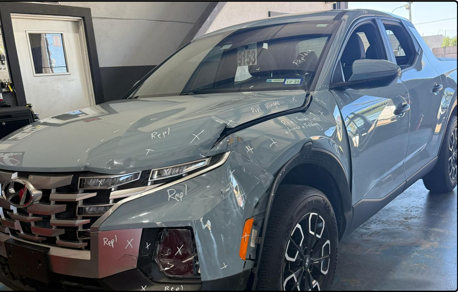 A light gray Hyundai Santa Cruz pickup truck with front-end collision damage parked inside a garage.