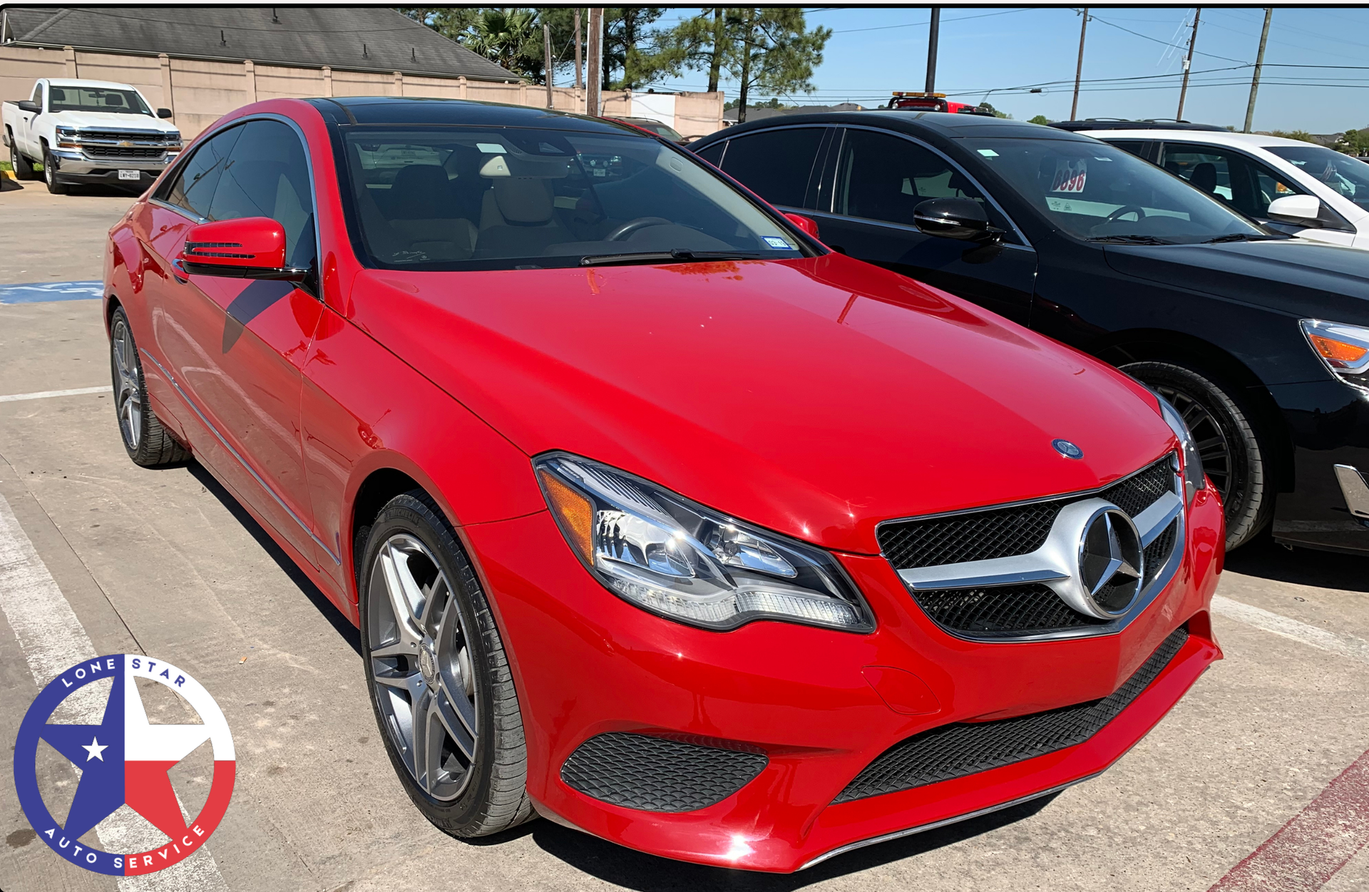 A red Mercedes-Benz coupe parked in a car lot on a sunny day.