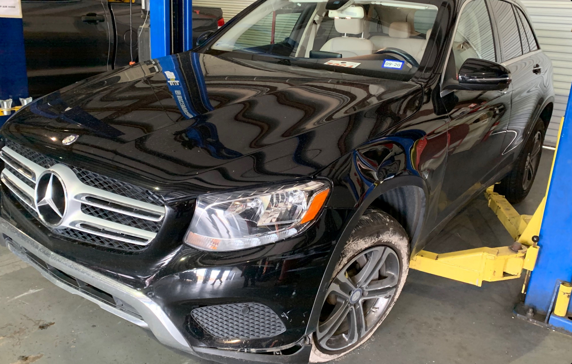 A black Mercedes-Benz SUV sits raised on a yellow automotive lift inside a repair shop.
