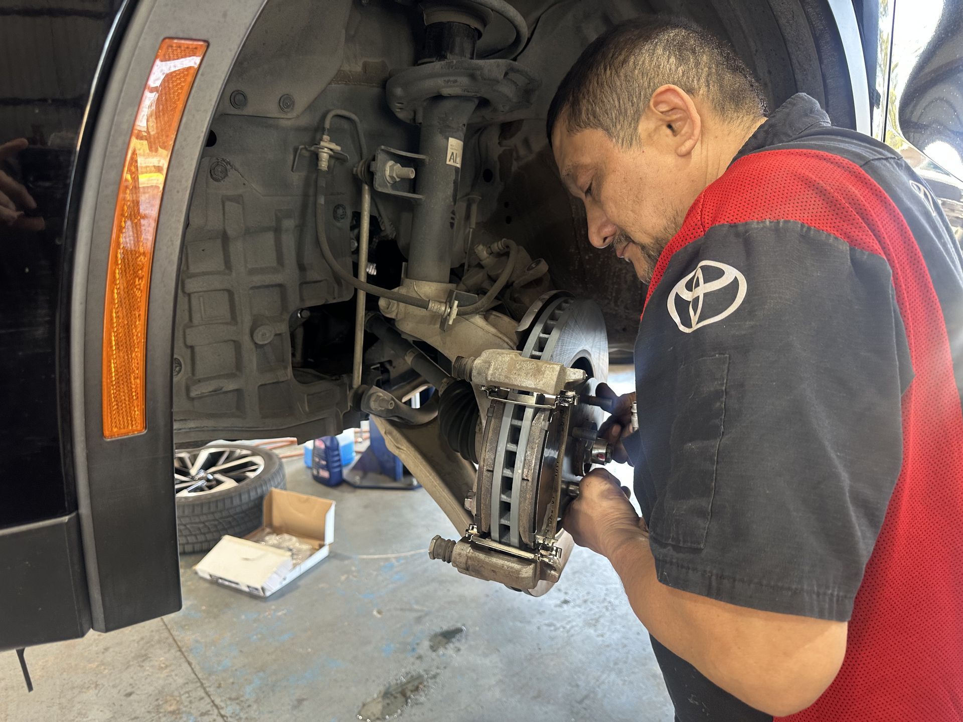 Mechanic working on the front wheel brake assembly of a black SUV in a garage