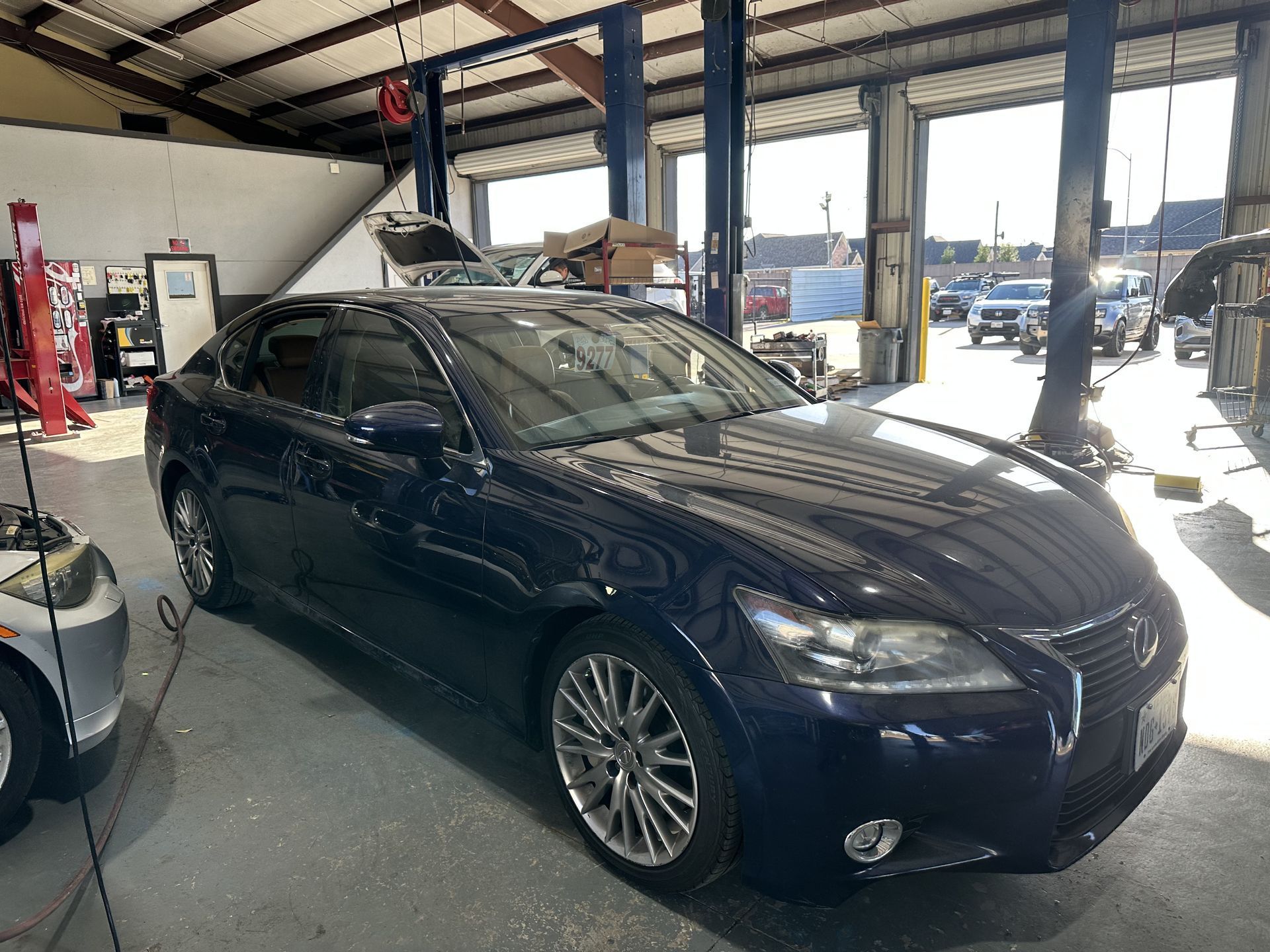 Dark blue sedan parked inside an auto garage with lifts and tools nearby