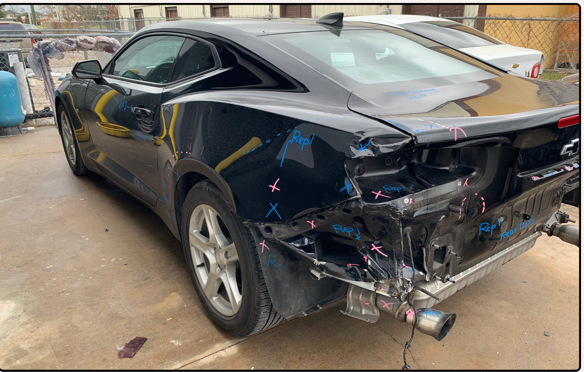 Black Chevrolet Camaro with significant rear-end collision damage in an outdoor salvage or repair lot.