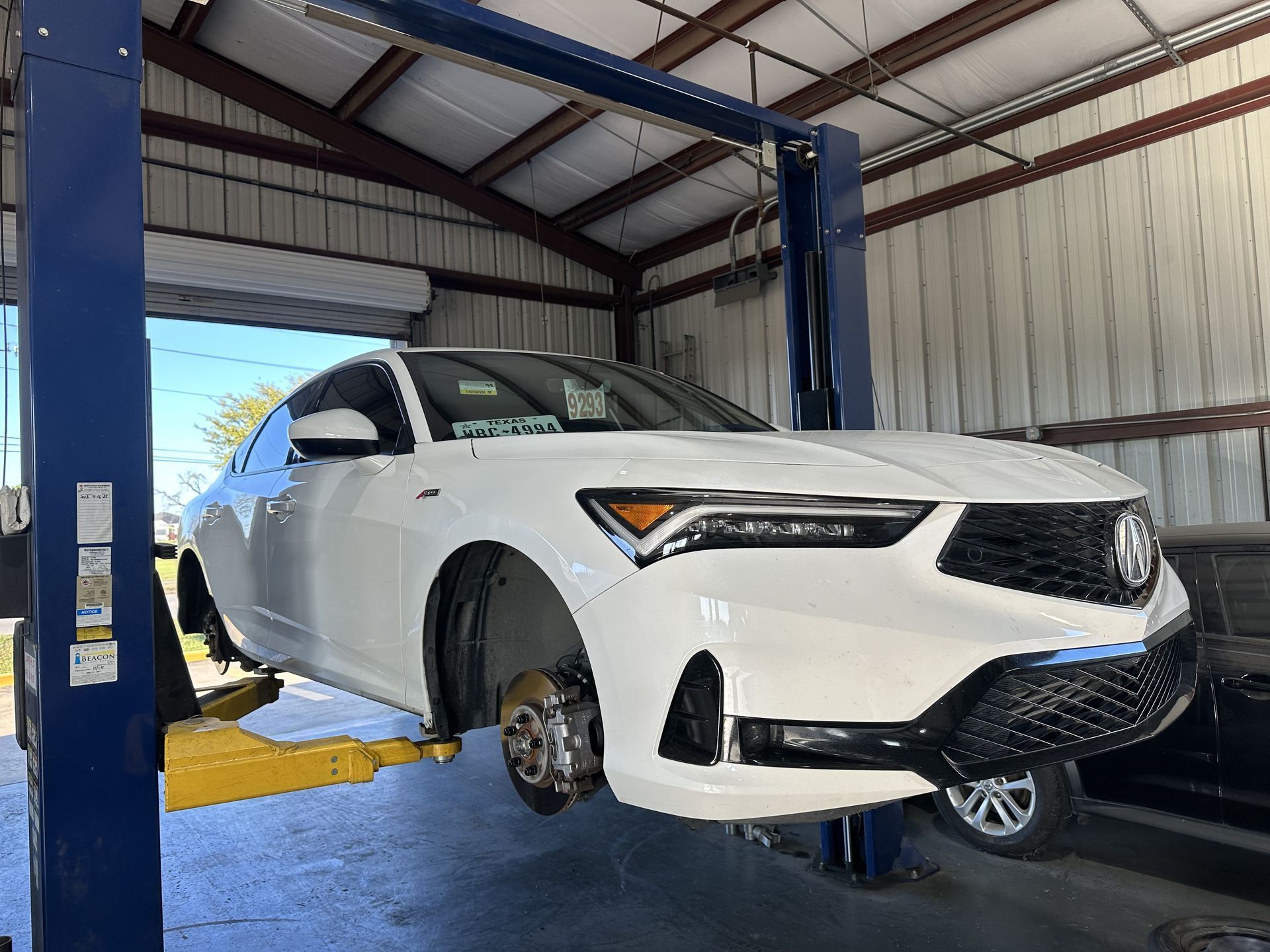 White sedan raised on a blue car lift inside an auto repair garage