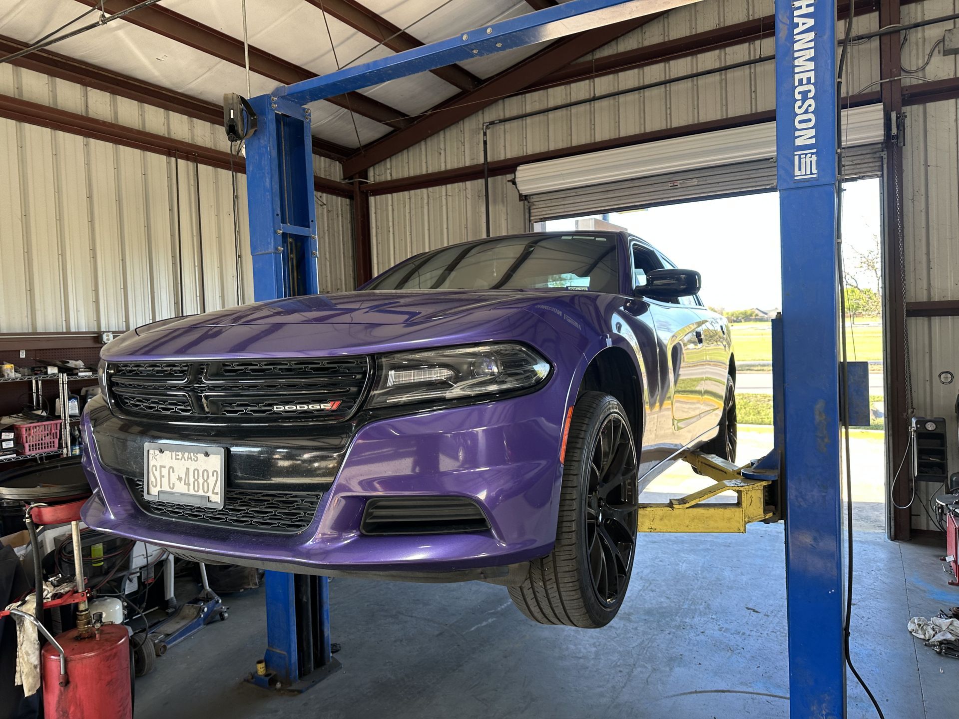 Purple Dodge Charger lifted on a blue car lift inside an auto shop, front wheels off the ground.