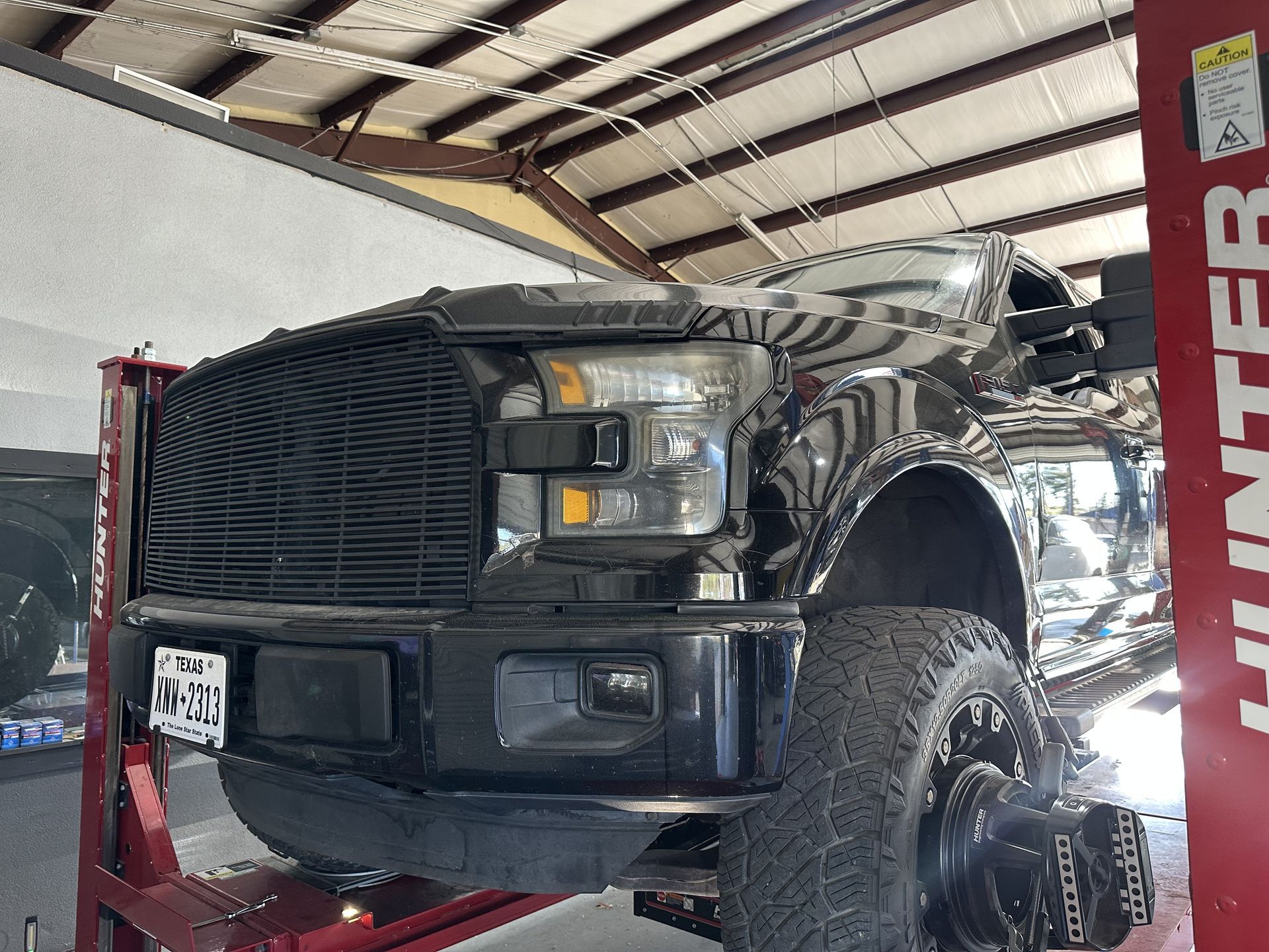 Black pickup truck lifted on a red hoist in a garage, front view with exposed wheel and bumper damage