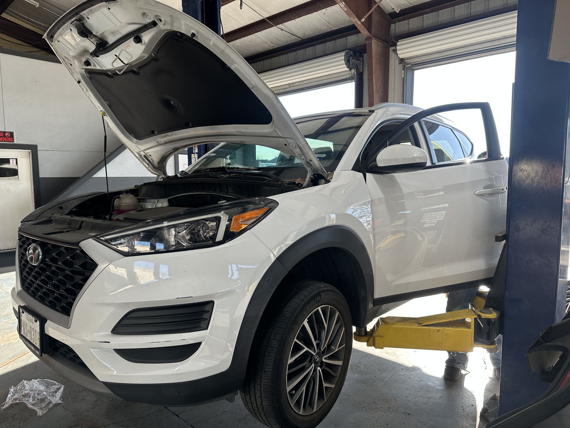 White SUV on a lift in an auto shop with hood and driver door open