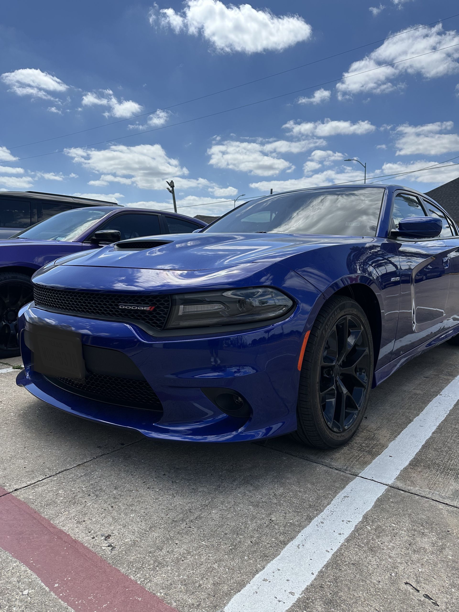 Blue sports car parked in a lot under a bright sky with scattered clouds.
