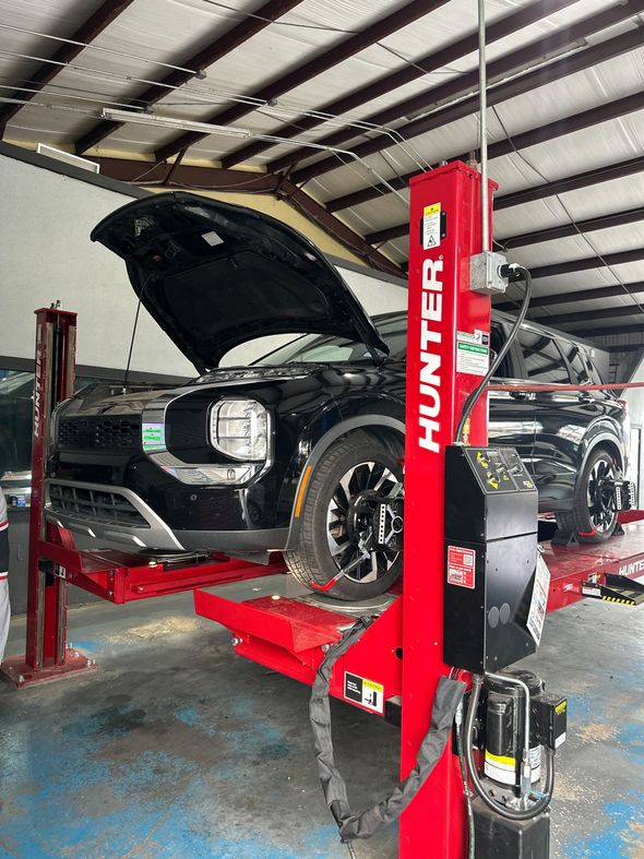 A black SUV with its hood open, lifted by a red Hunter automotive service rack inside a mechanic shop.