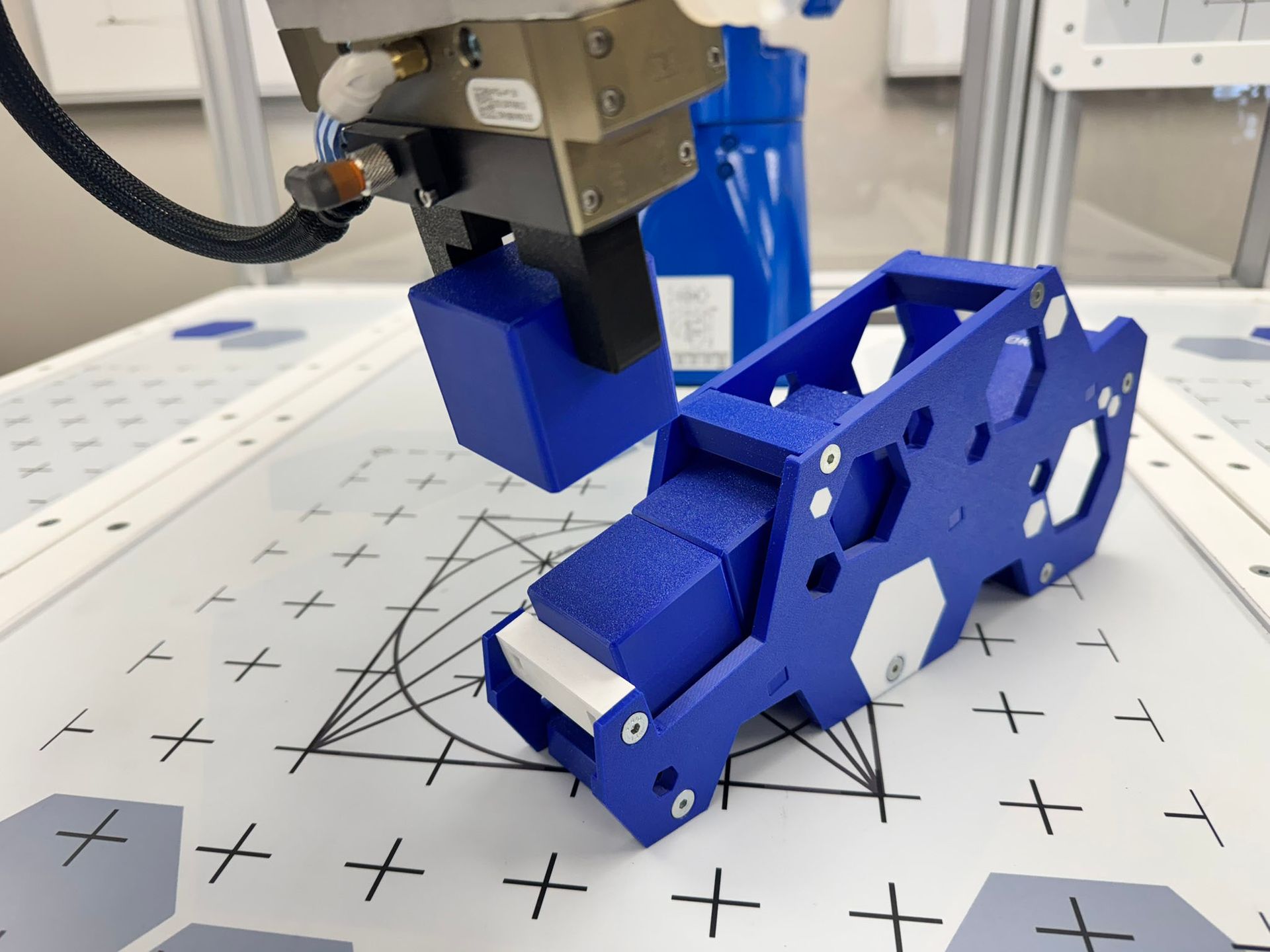 Blue robotic gripper working on a blue 3D-printed part on a marked lab work surface.