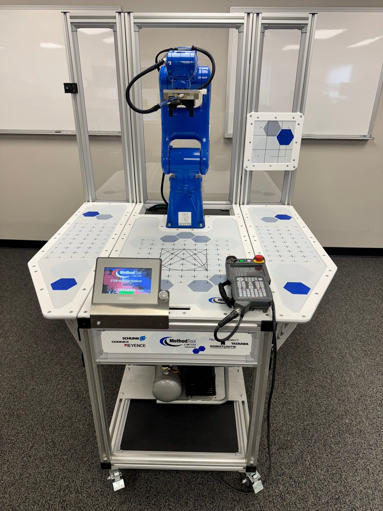 Industrial robot arm on a lab workbench with a small screen, control keypad, and wiring.
