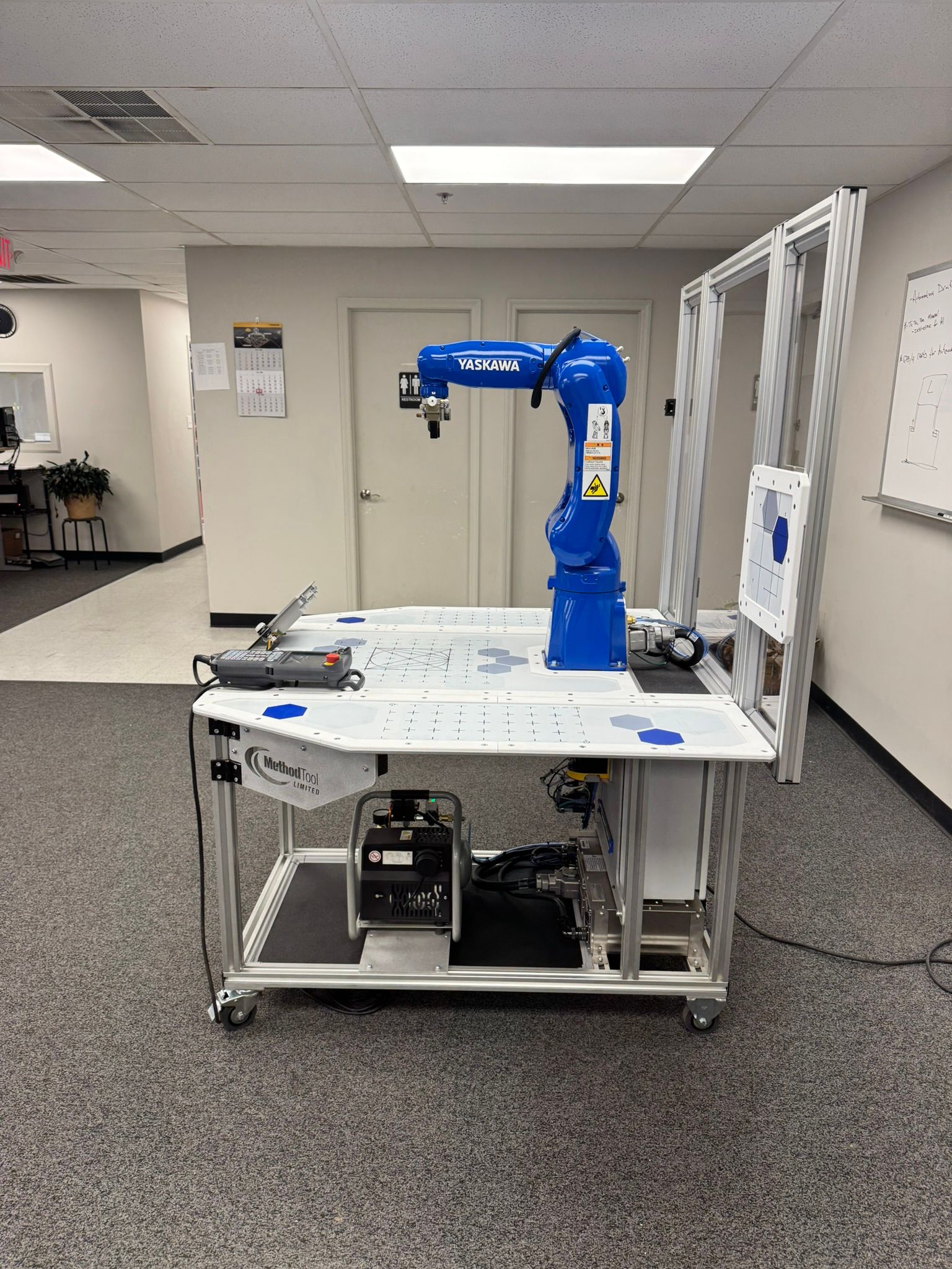 Blue robotic arm on a wheeled workbench in a lab or workshop room.