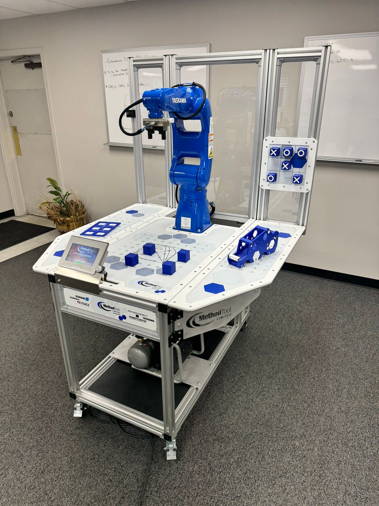 Blue industrial robot arm on a wheeled workstation in a lab or workshop, surrounded by control panels.