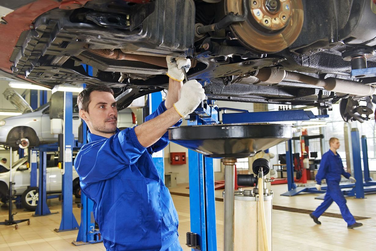 Mechanic in blue coveralls working under a raised car in an auto repair shop