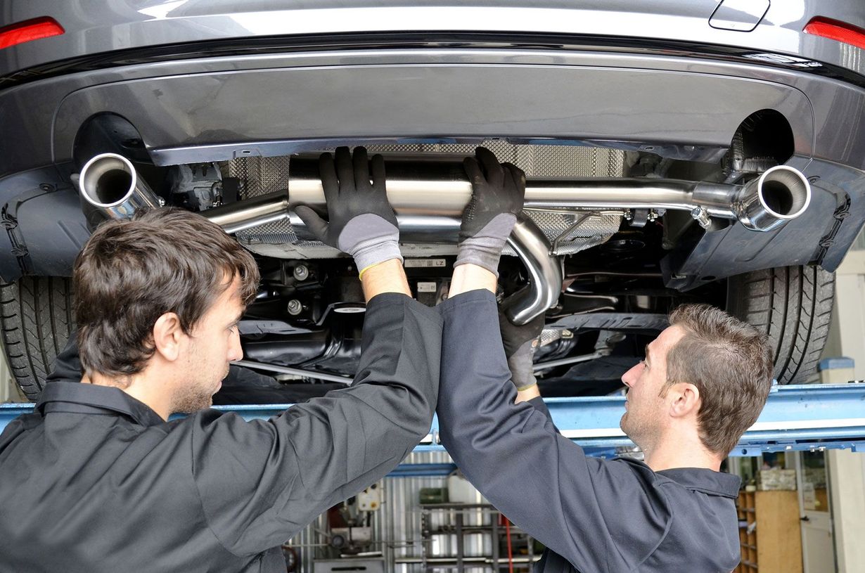 Two mechanics inspecting a car’s exhaust system on a lift in an auto shop