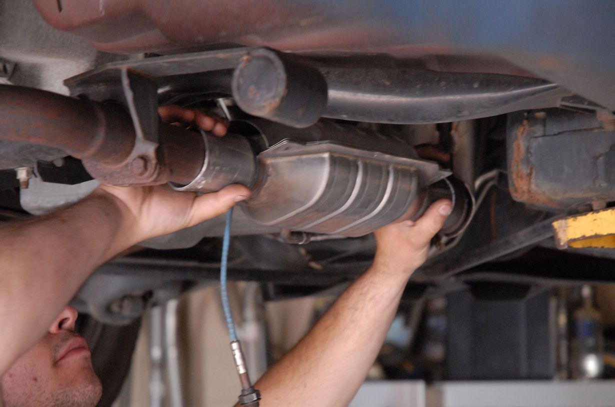 Mechanic installing a car’s exhaust pipe under the vehicle