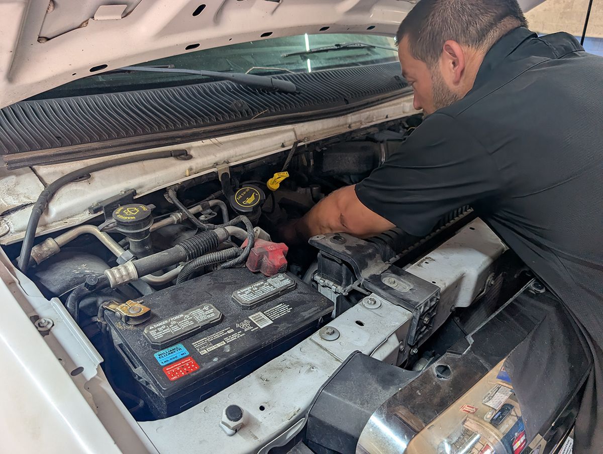 Mechanic working under the hood of a car, inspecting the engine bay.
