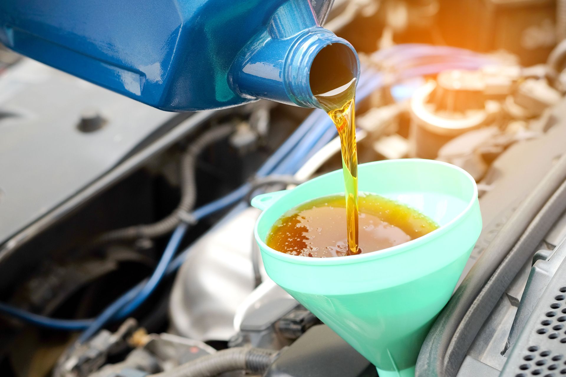 Oil being poured from a blue bottle into a green funnel in a car engine bay.