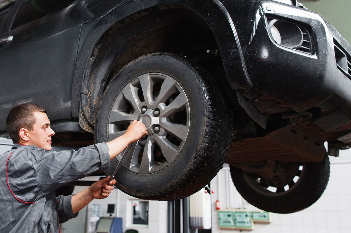 Mechanic tightening lug nuts on a raised black car wheel in an auto shop