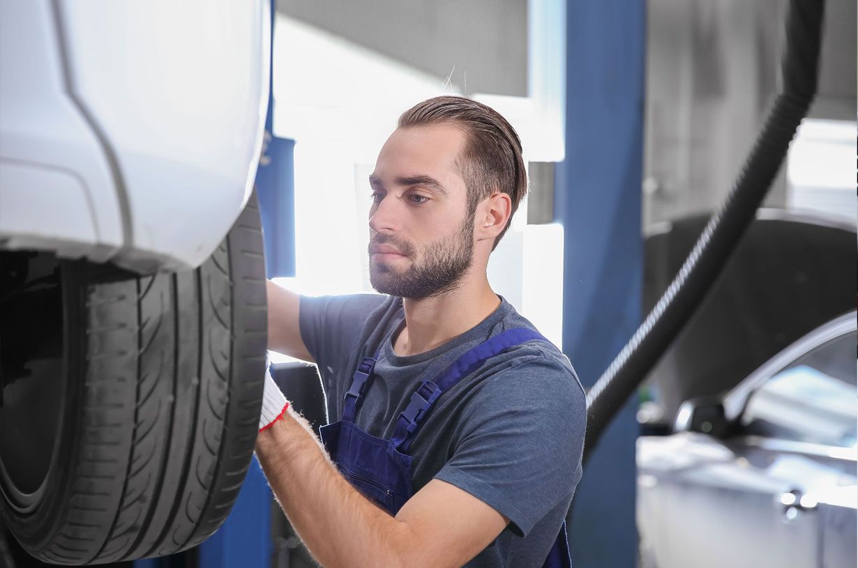 Mechanic inspecting a car tire in a garage, wearing a blue shirt and gloves