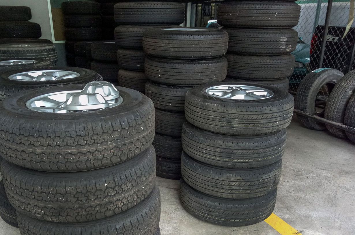 Stacks of tires with silver hubcaps stored outdoors beside a chain-link fence.