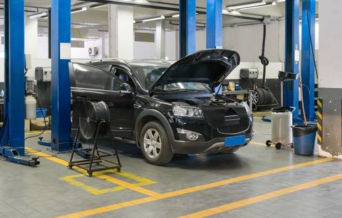 Black SUV in an auto repair shop with hood open, surrounded by service equipment and blue lifts.