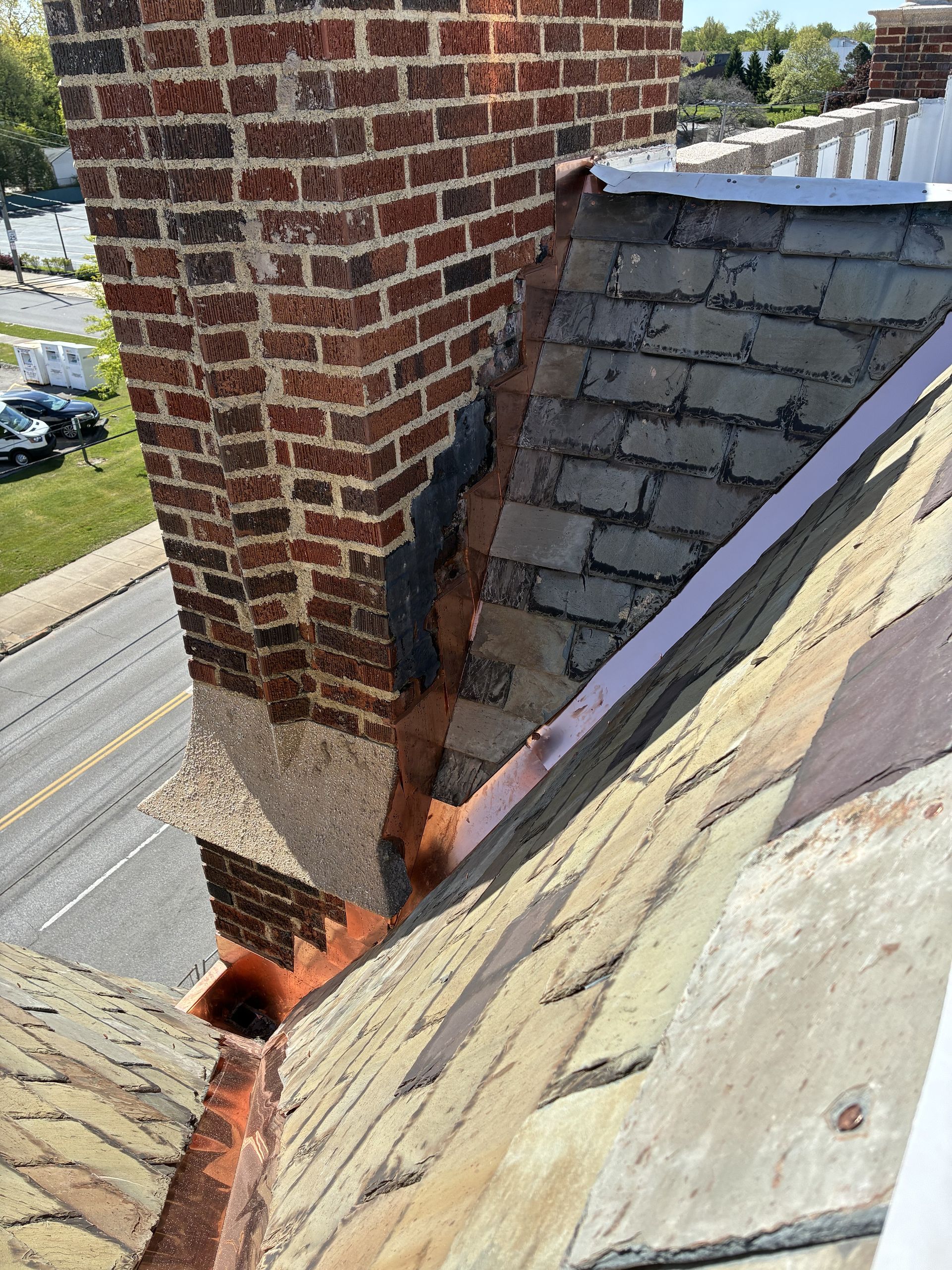 Damaged roof with a brick chimney and missing shingles, exposing the roof deck and flashing.