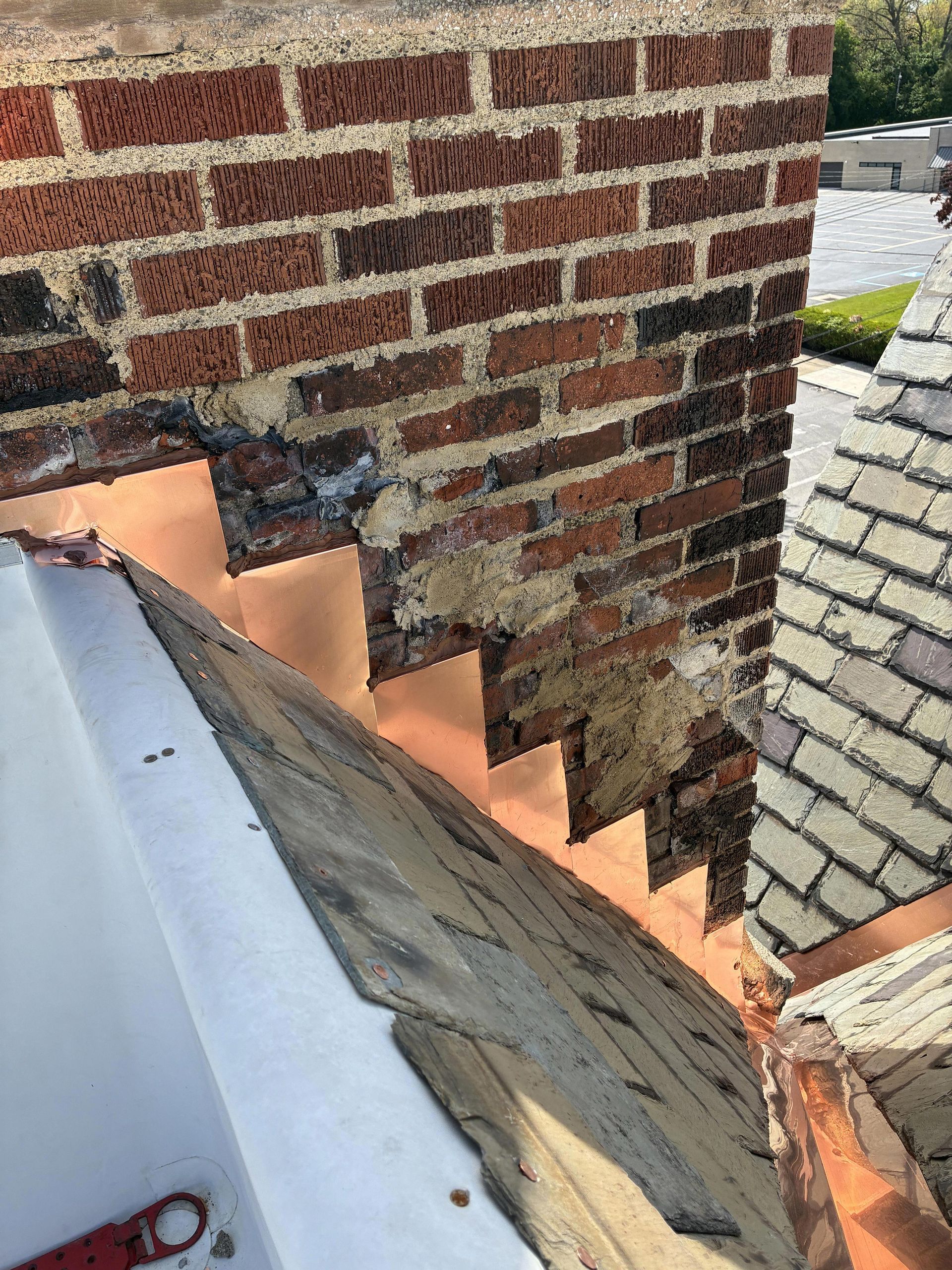 Brick chimney with damaged flashing and exposed roof shingles on a rooftop corner