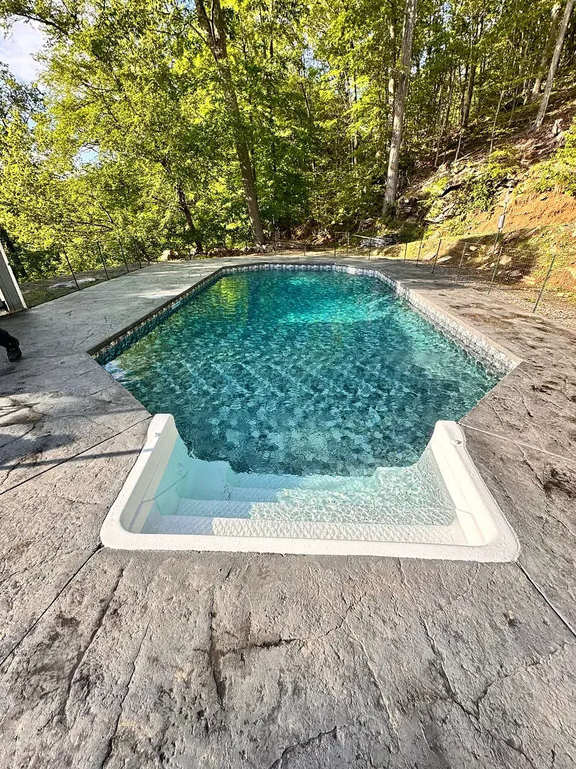 Small backyard pool with blue water, surrounded by trees and stone decking.