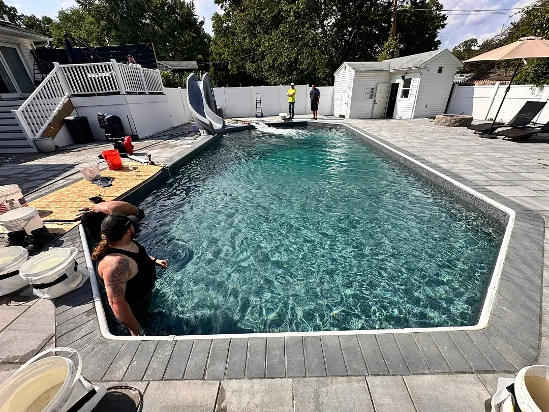 Backyard swimming pool with two people relaxing on the edge and lounge chairs nearby