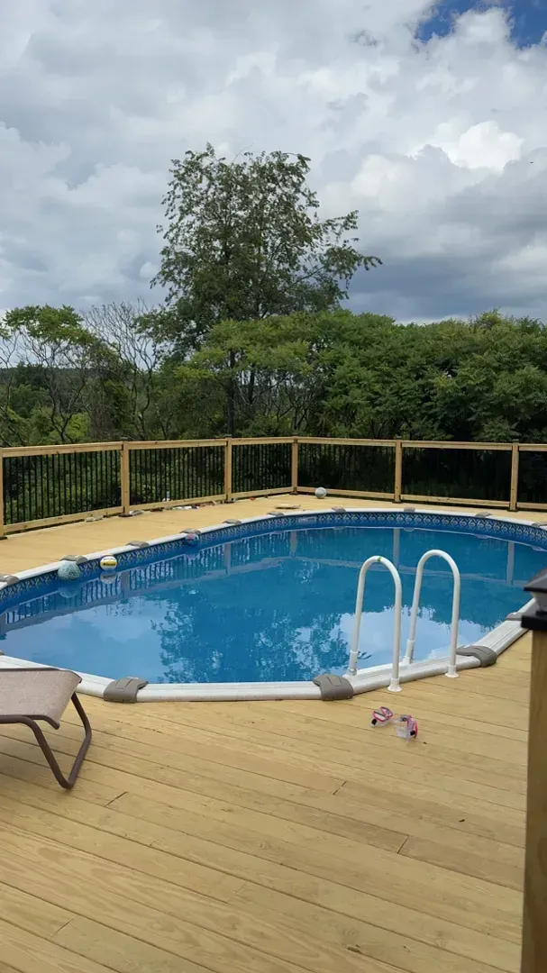 Backyard pool with blue water, wooden deck, white railing, lounge chair, and cloudy sky