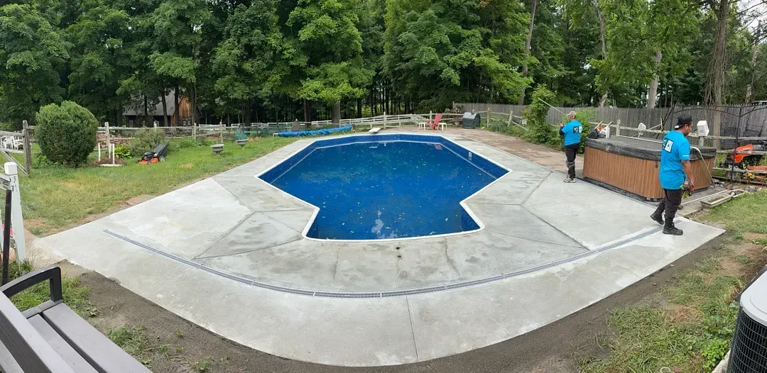 Outdoor pool drained for maintenance, with two workers standing nearby in blue shirts